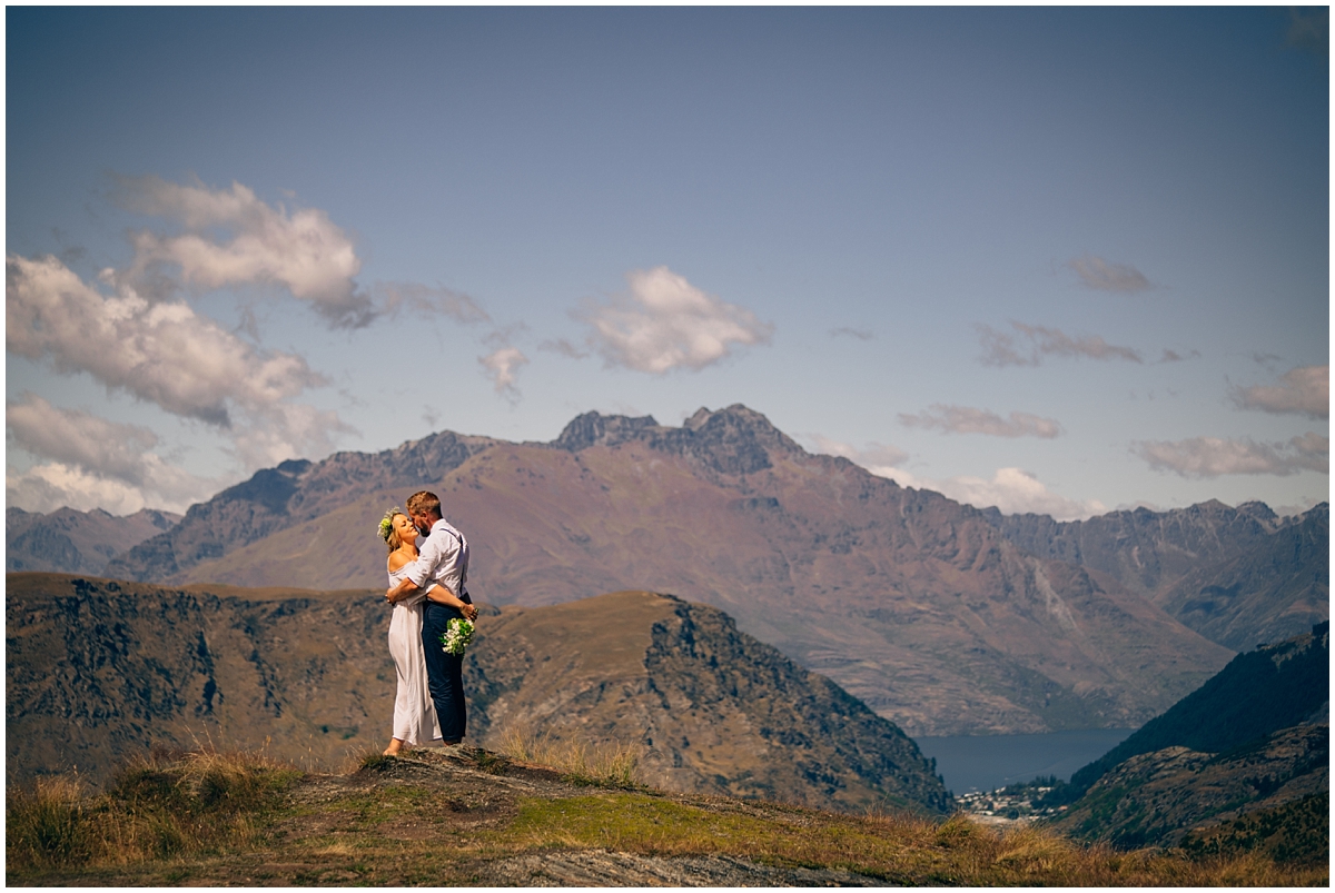 Bride and groom kiss on a hilltop with a mountain backdrop
