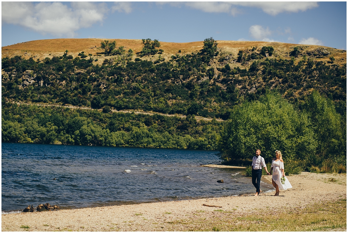 Bride and groom walk along the shore of Lake Hayes