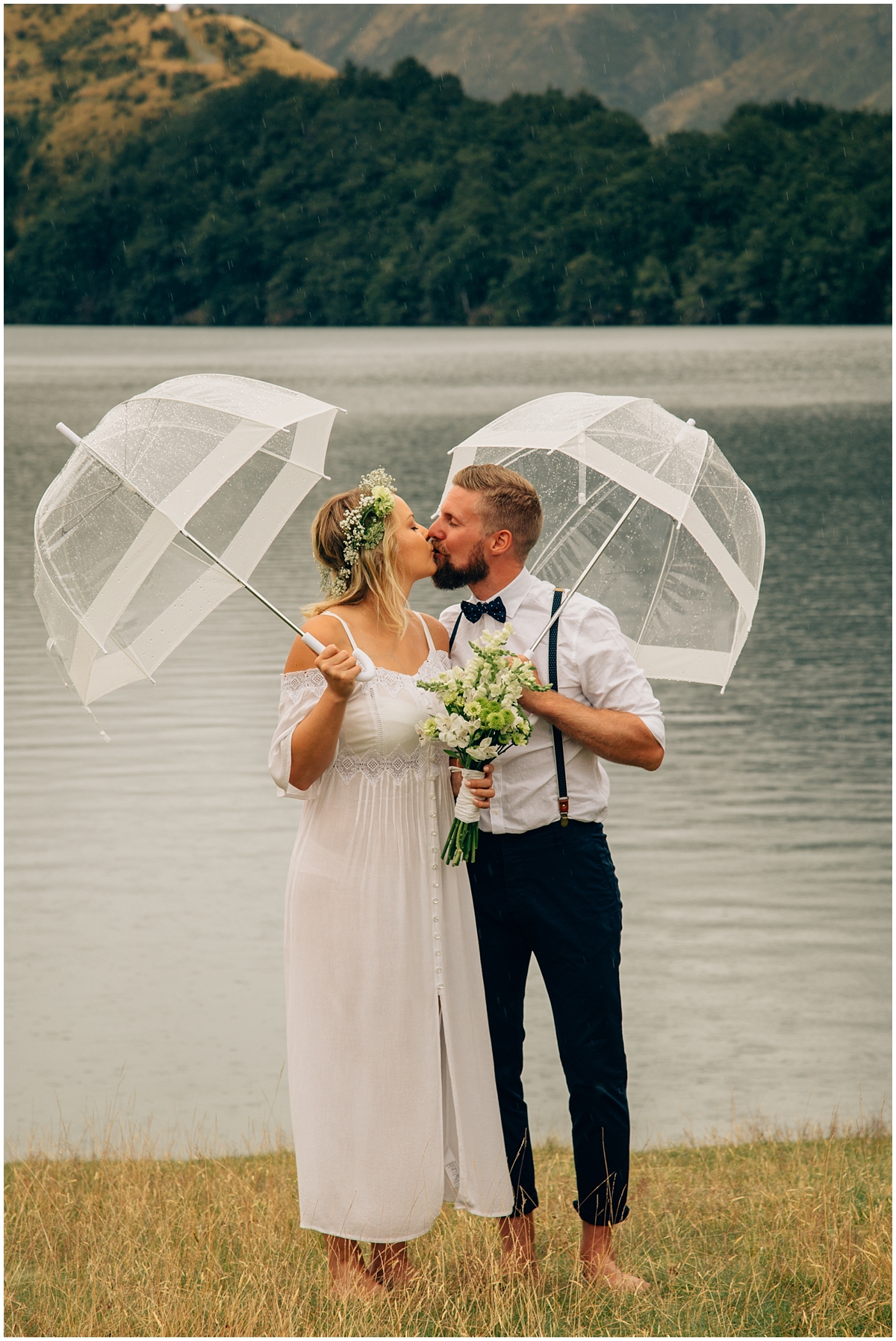 Bride and groom kiss at water's edge under umbrellas
