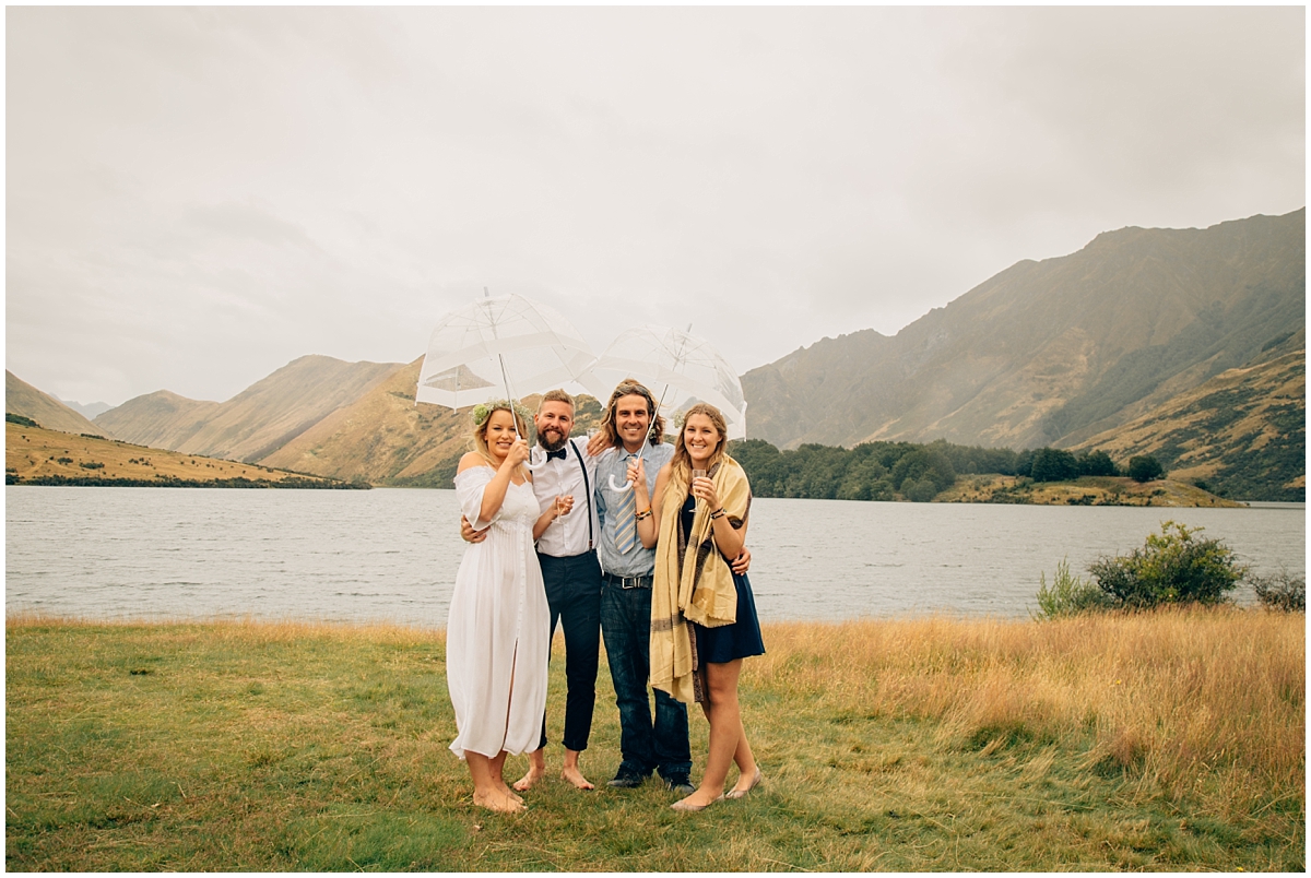 Bride and groom stand under umbrellas with friends at Queenstown elopement