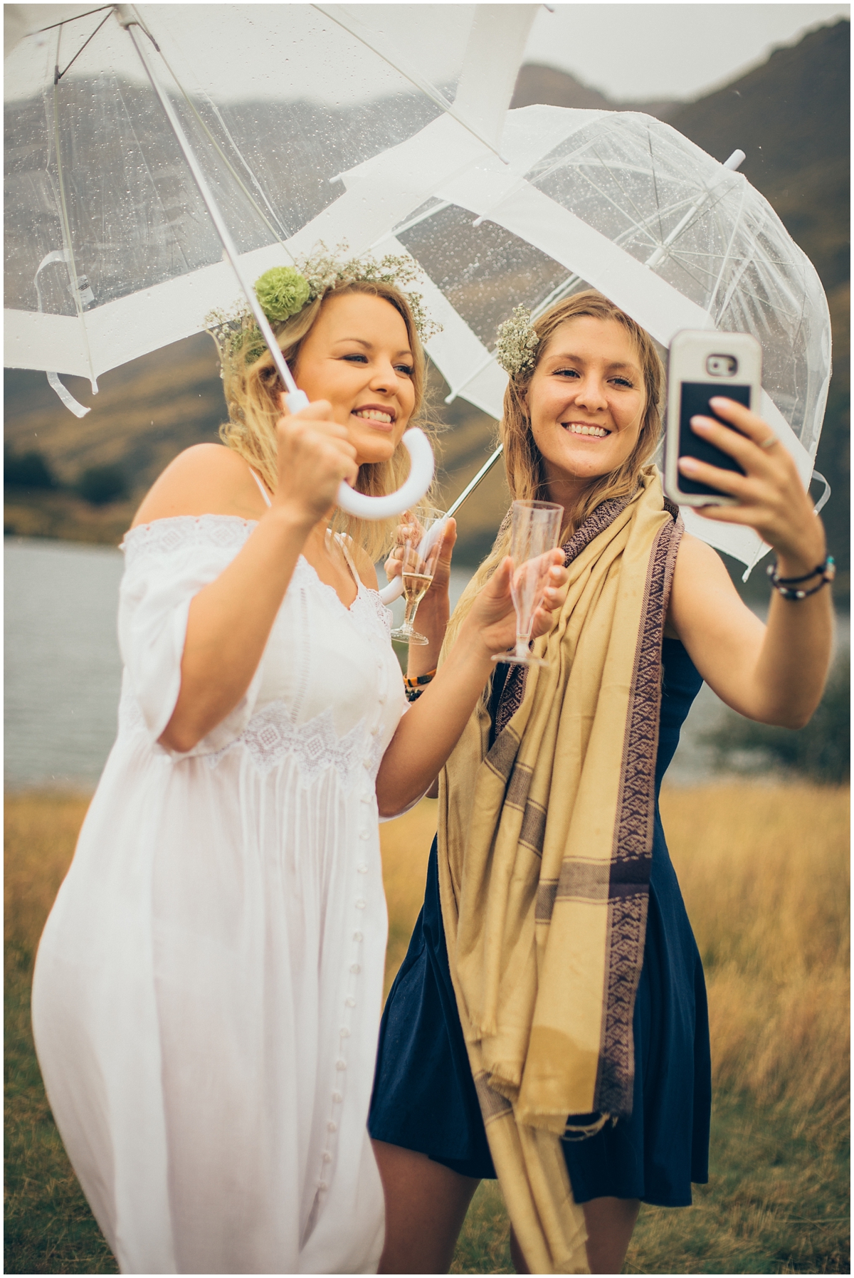 Bride and her friend take a selfie in the rain under umbrellas