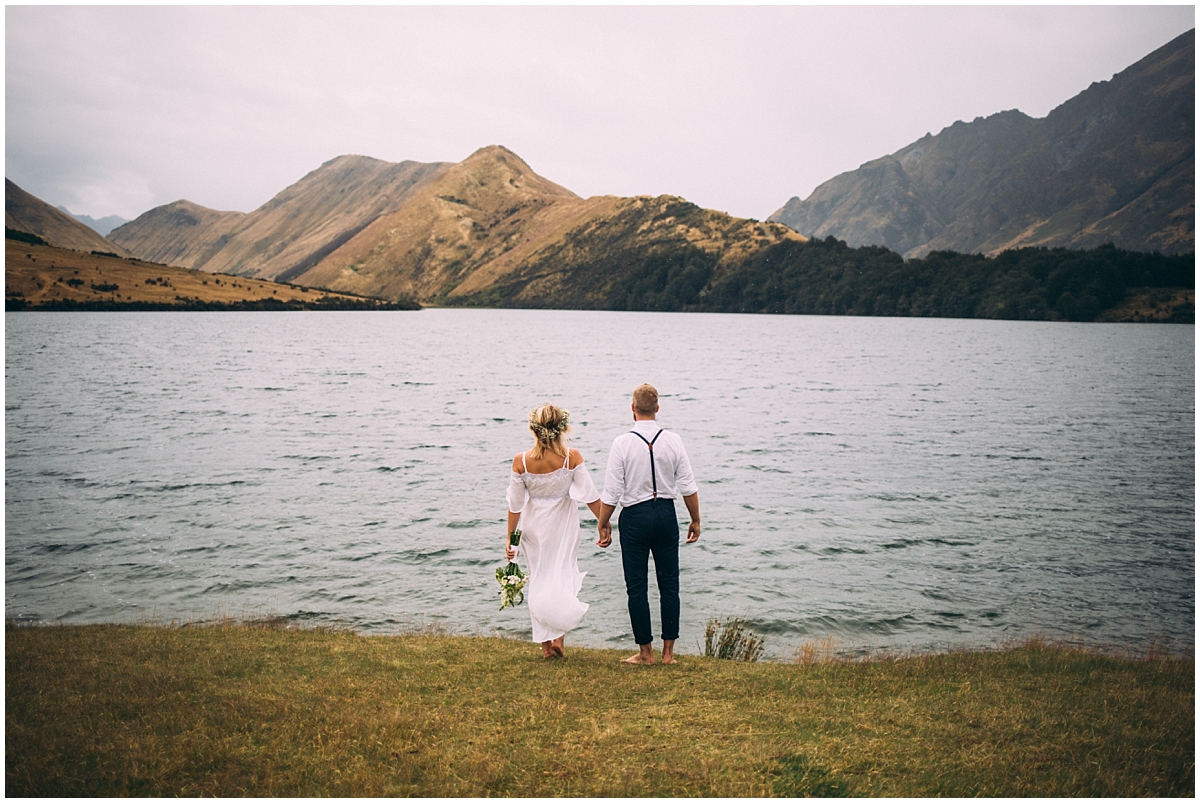 Bride and groom standing at the water's edge gazing at mountains