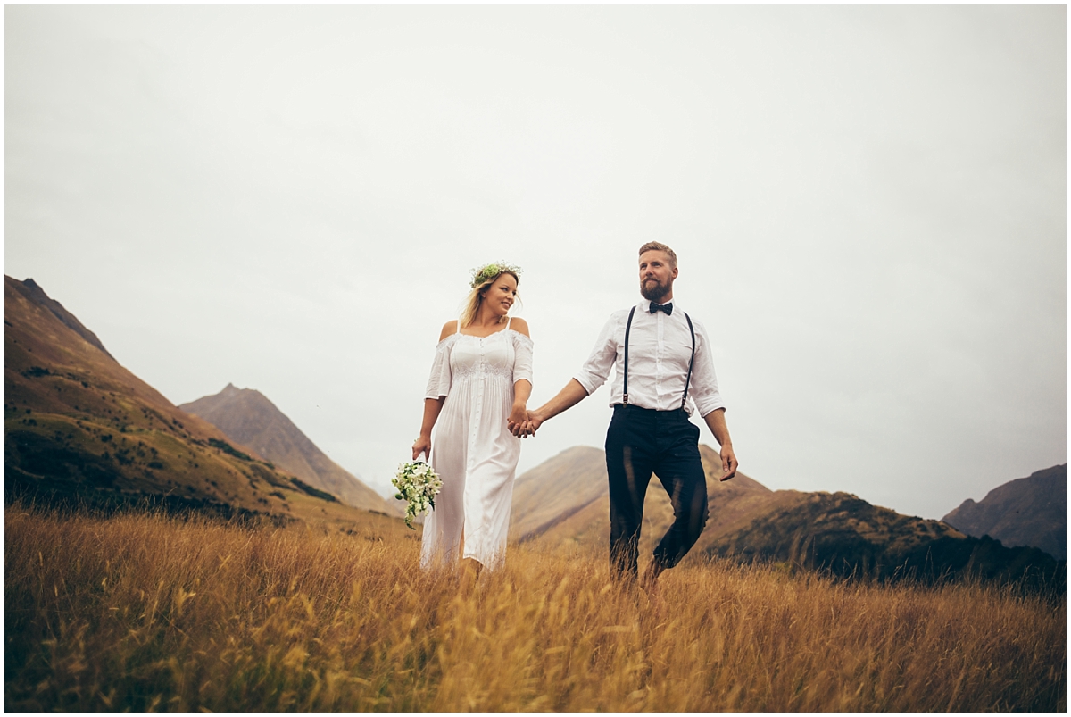 Bride and groom walk through a field with a mountain backdrop