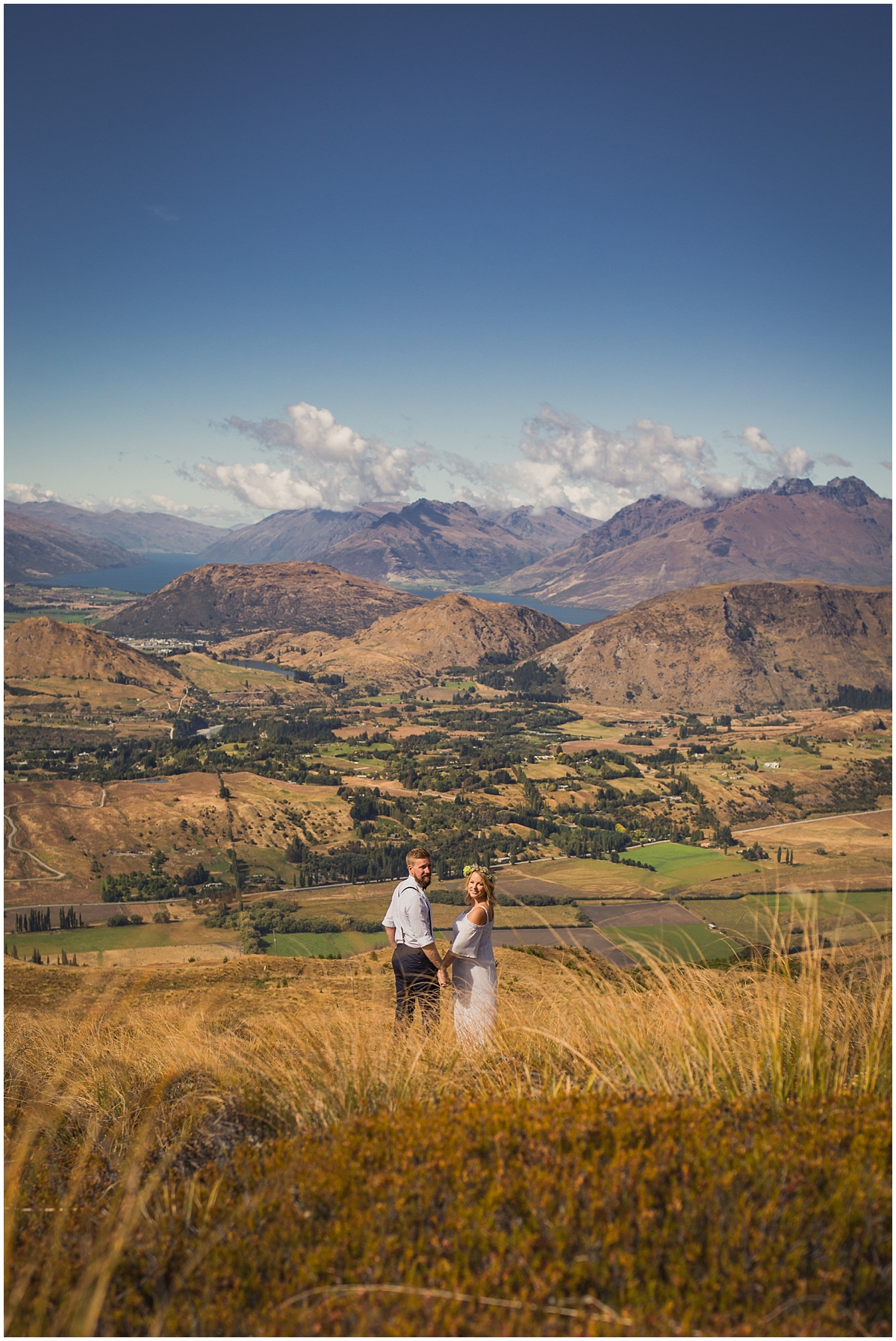 Bride and groom stand on a hillside looking out at lake and mountain view